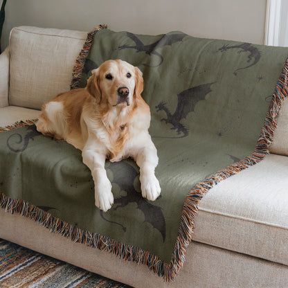 A golden retriever dog is lying on a green blanket with a dragon design, resting on a white couch.