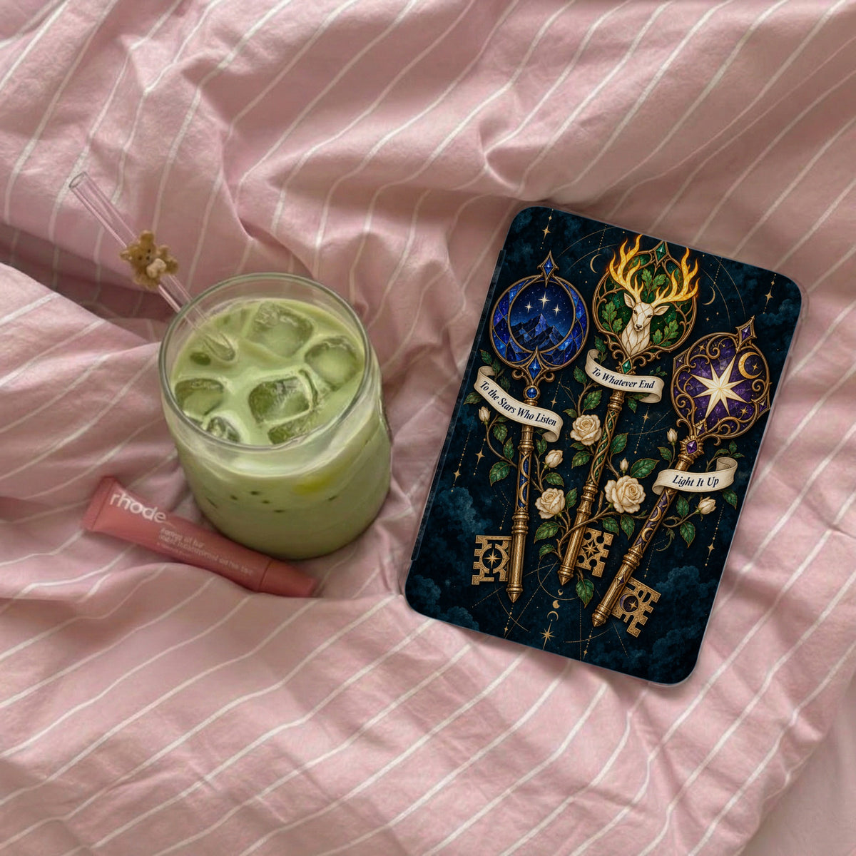 Artistic keys with celestial designs and quotes on a dark background, next to a drink and lip balm.
