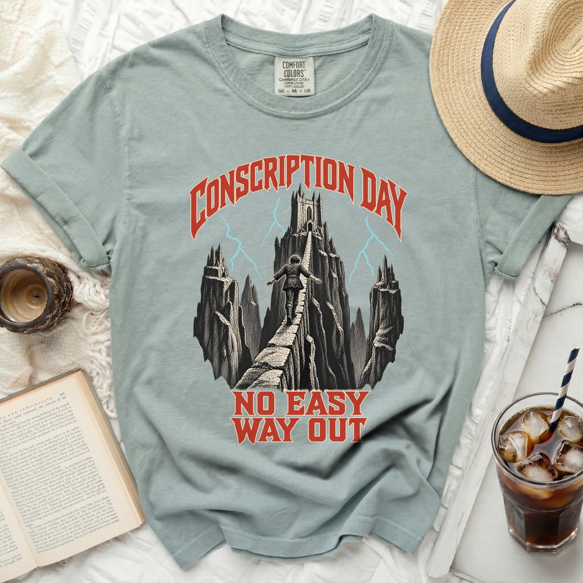 Sage green t-shirt featuring a graphic of a person walking a narrow bridge toward a distant castle under the text Conscription Day and No Easy Way Out.