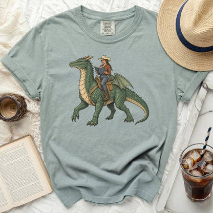 Green dragon with a woman in a cowboy hat reading a book while riding.