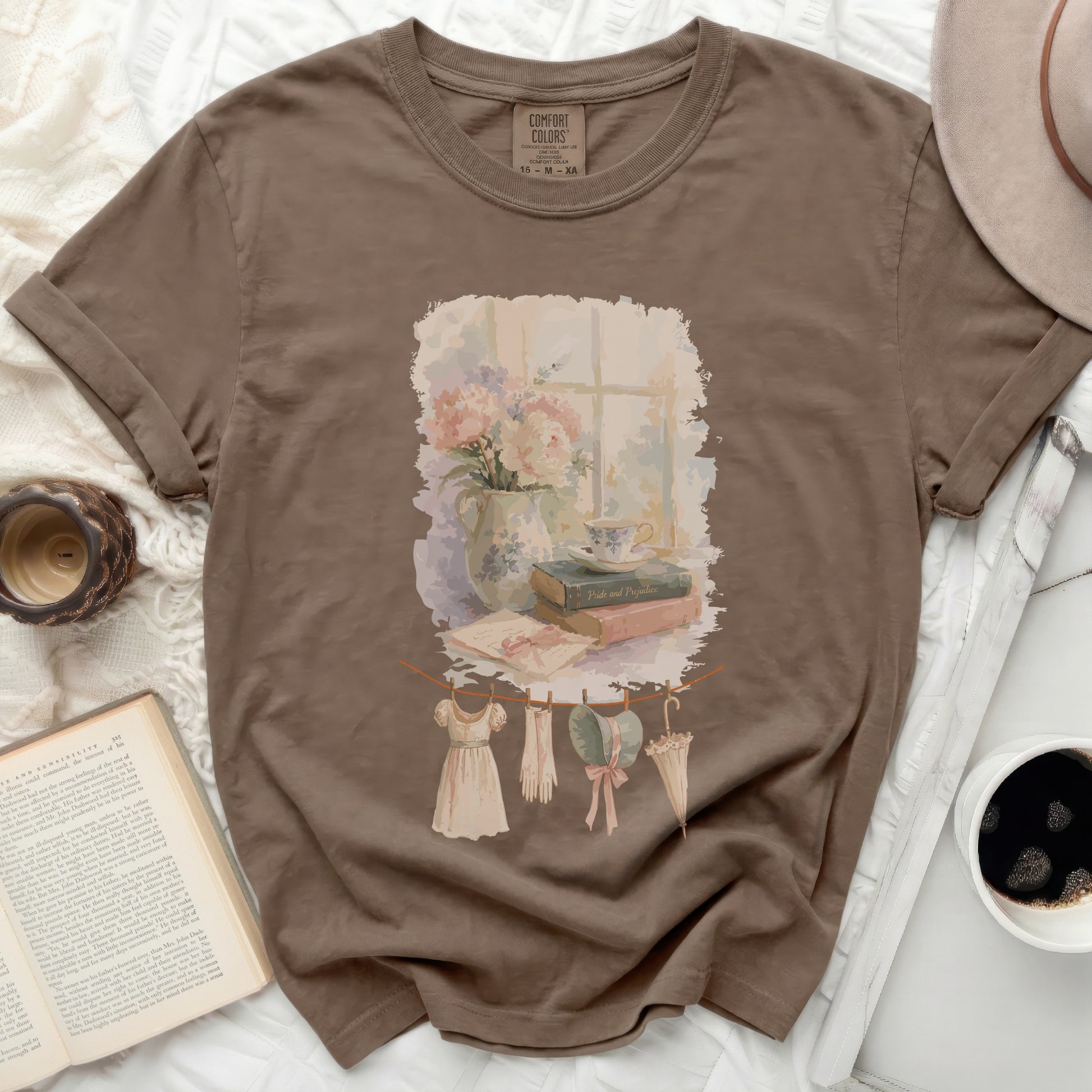 Brown t-shirt with a watercolor graphic of a window, flowers, books, and clothes on a clothesline.