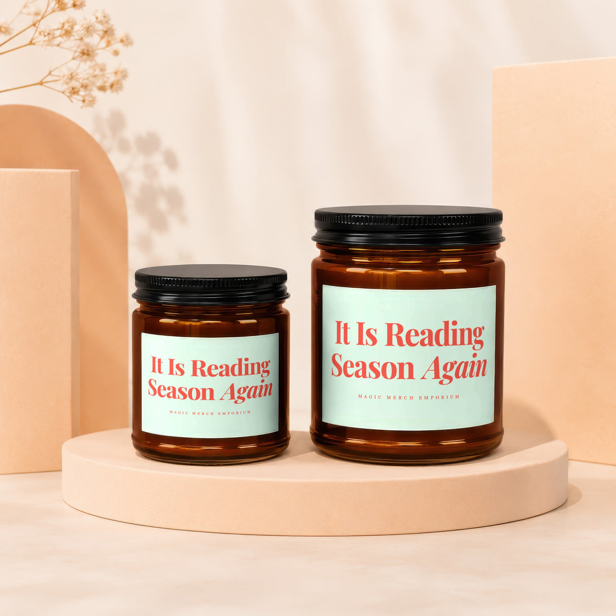 Two amber glass candles with black lids, reading "It Is Reading Season Again".