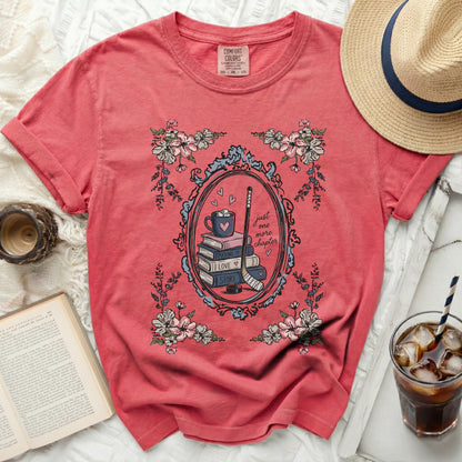 Coral t-shirt with oval frame of flowers and hockey gear, text "just one more chapter"