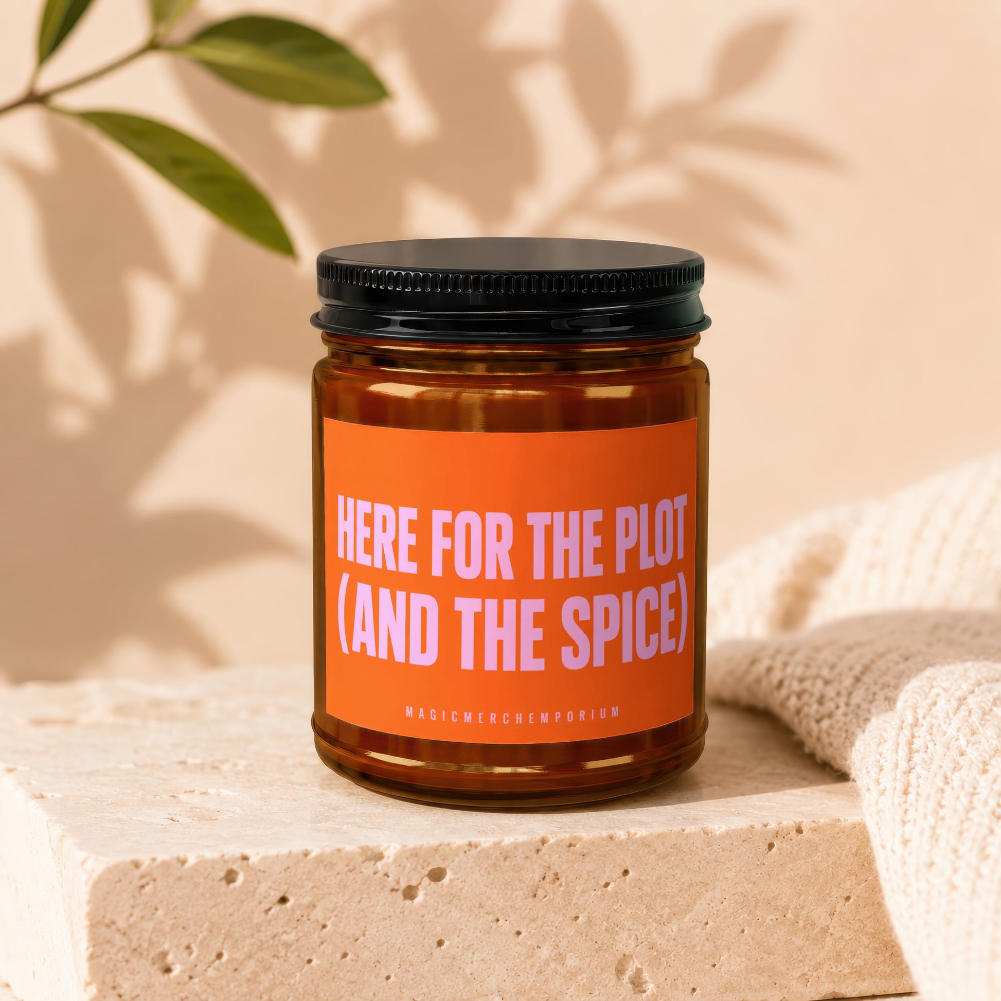 Amber jar candle with orange label text "HERE FOR THE PLOT (AND THE SPICE)".