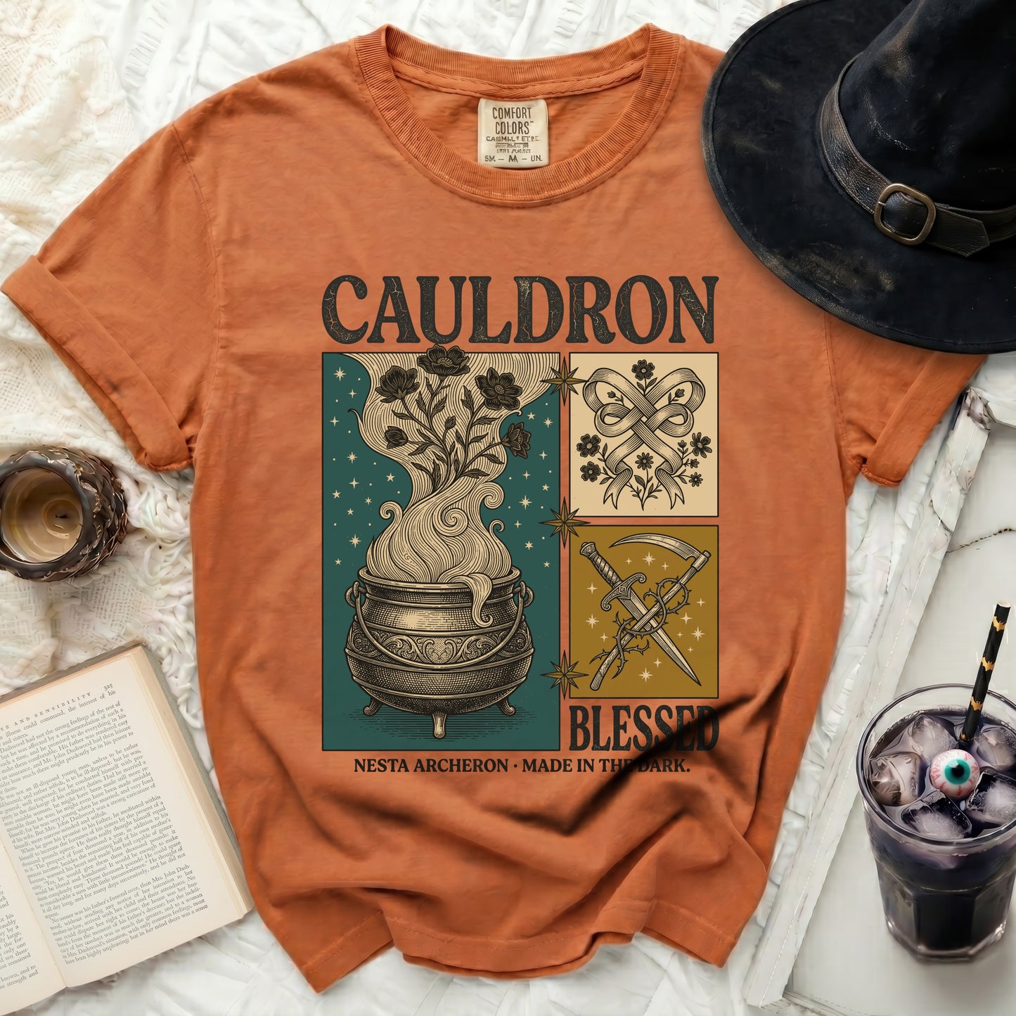 Orange t-shirt with "Cauldron Blessed" graphic featuring a cauldron, flowers, and scythe.