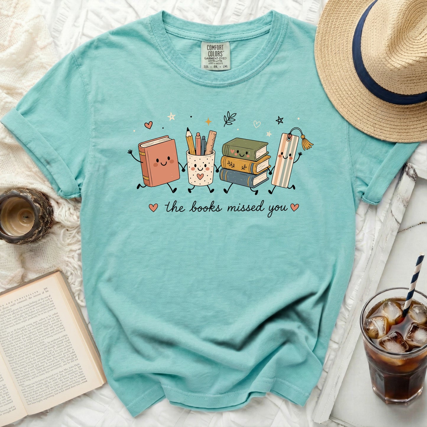 Aqua t-shirt with cartoon books, pencil cup, and bookmark holding hands, saying "the books missed you".