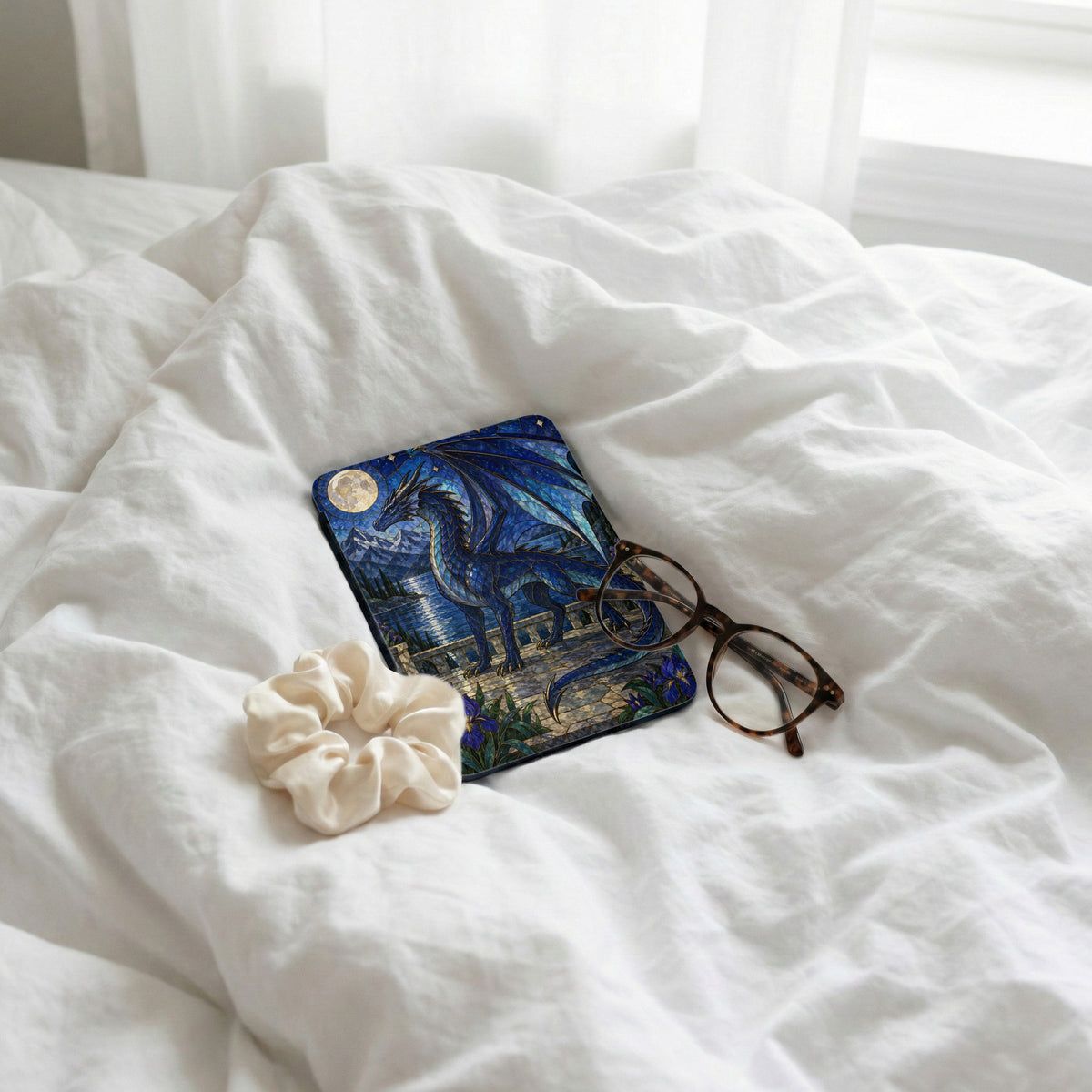 Blue dragon art on a case with glasses and scrunchie on white bedding.