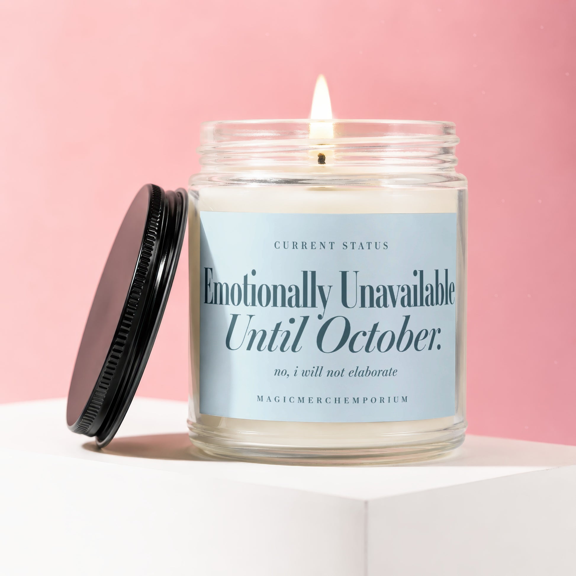 Glass jar candle with lit wick, label reads "Emotionally Unavailable Until October."