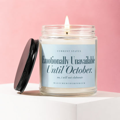 Glass jar candle with lit wick, label reads "Emotionally Unavailable Until October."