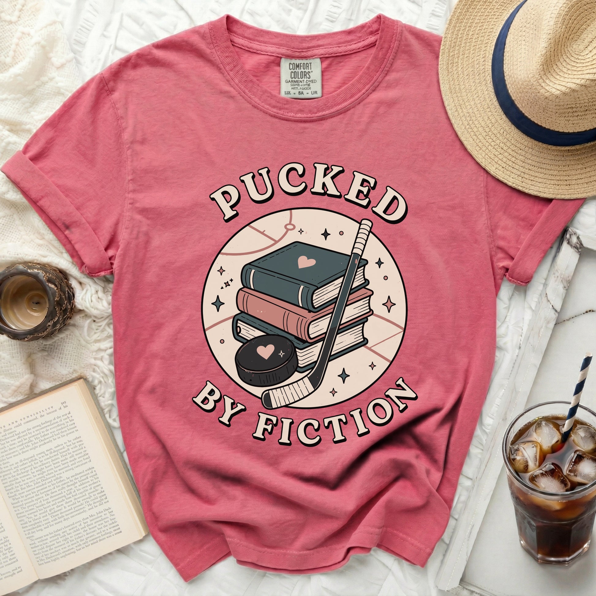 Pink t-shirt with books, hockey puck, and text "Pucked By Fiction".