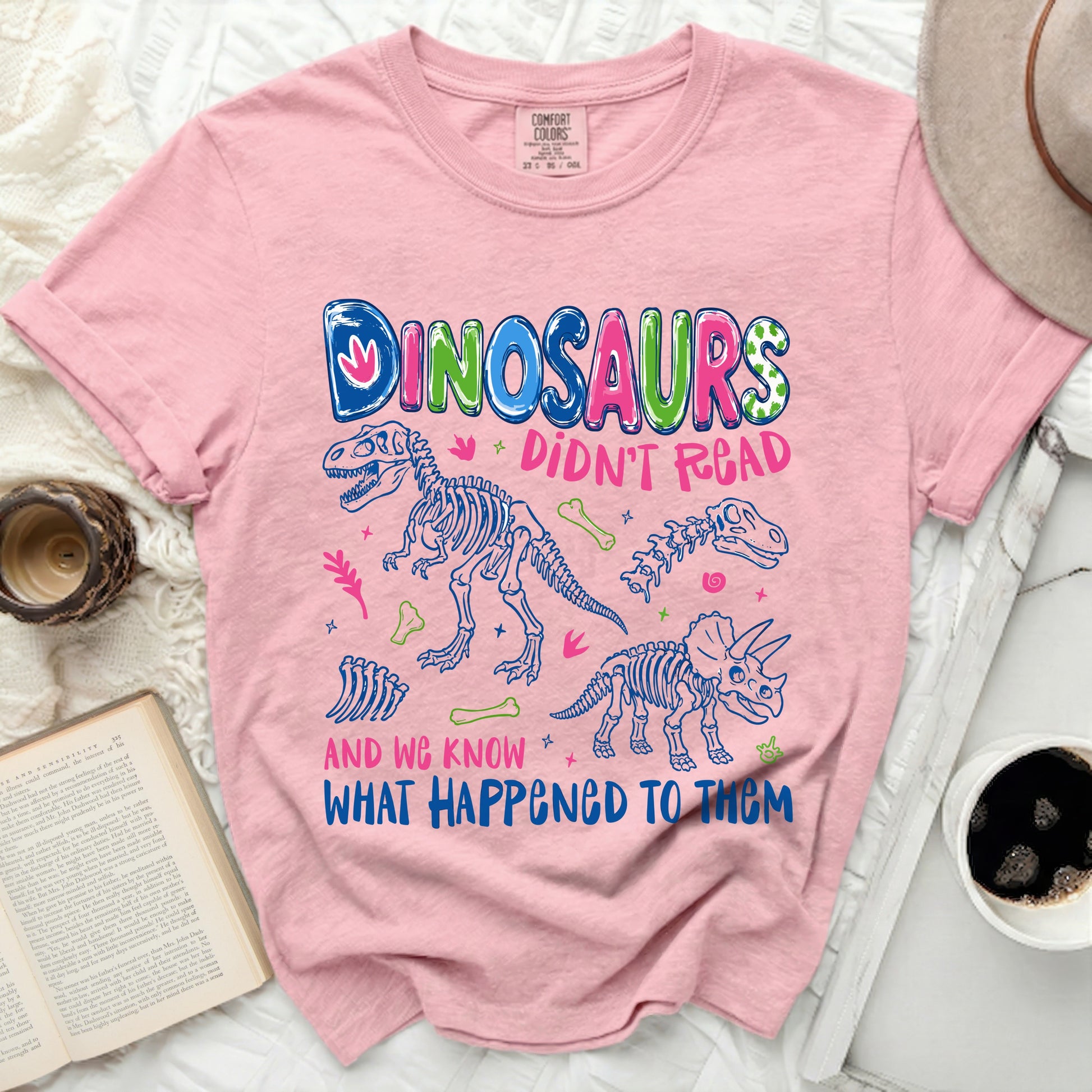 Pink t-shirt with "DINOSAURS DIDN'T READ AND WE KNOW WHAT HAPPENED TO THEM" text and graphics.