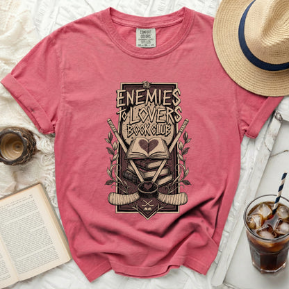 Pink t-shirt with "The Enemies to Lovers Book Club" graphic and hockey gear.