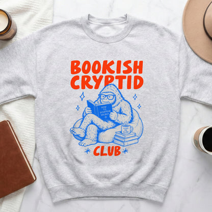 Grey sweatshirt with "Bookish Cryptid Club" text and illustration of Bigfoot reading.
