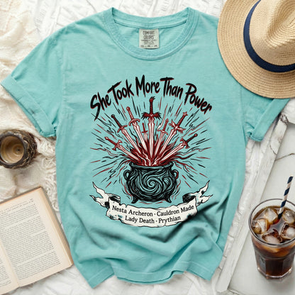 Teal shirt with a cauldron, swords, and text "She Took More Than Power".