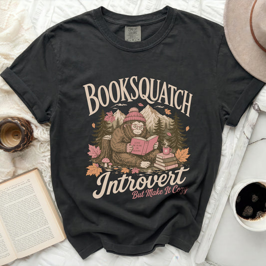 Black t-shirt with a graphic of a reading Bigfoot saying "Booksquatch Introvert But Make It Cozy."
