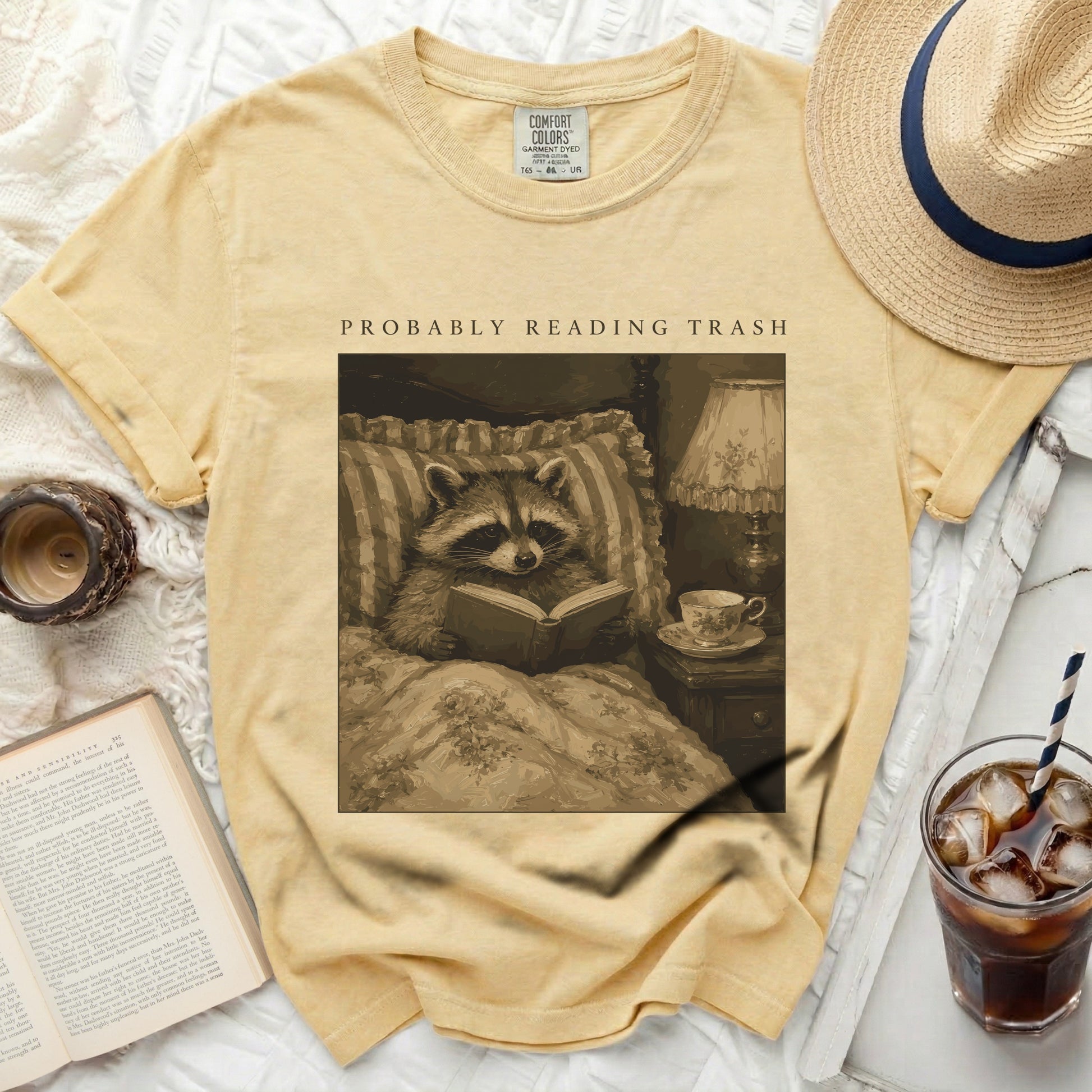 T-shirt with a graphic of a raccoon reading in bed and the text "PROBABLY READING TRASH."