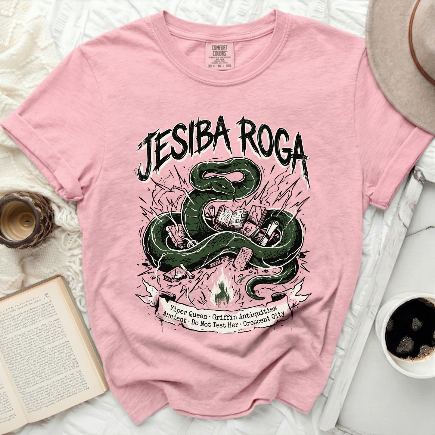 Pink t-shirt with green snake and books graphic, "JESIBA ROGA" text.