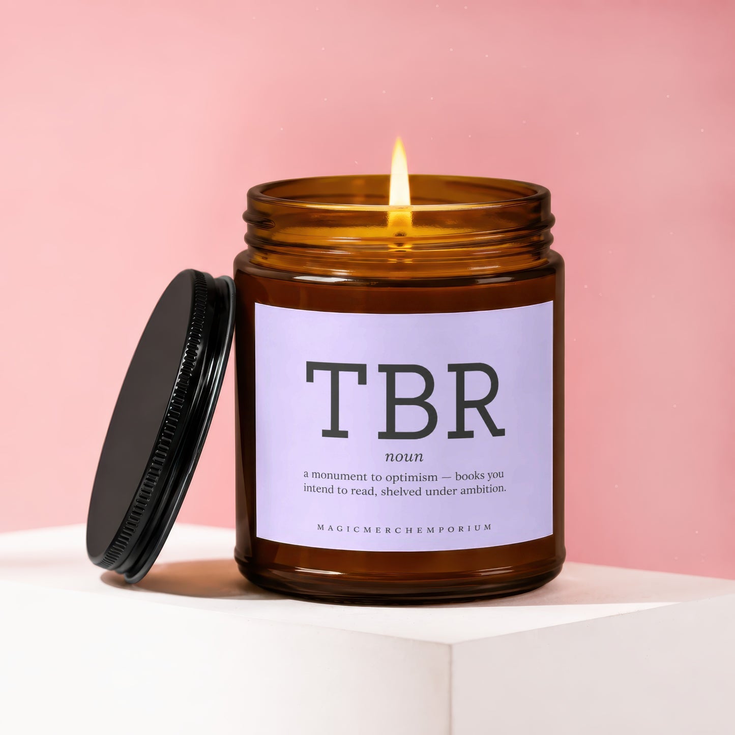 Amber candle with lit flame, labeled "TBR noun a monument to optimism".