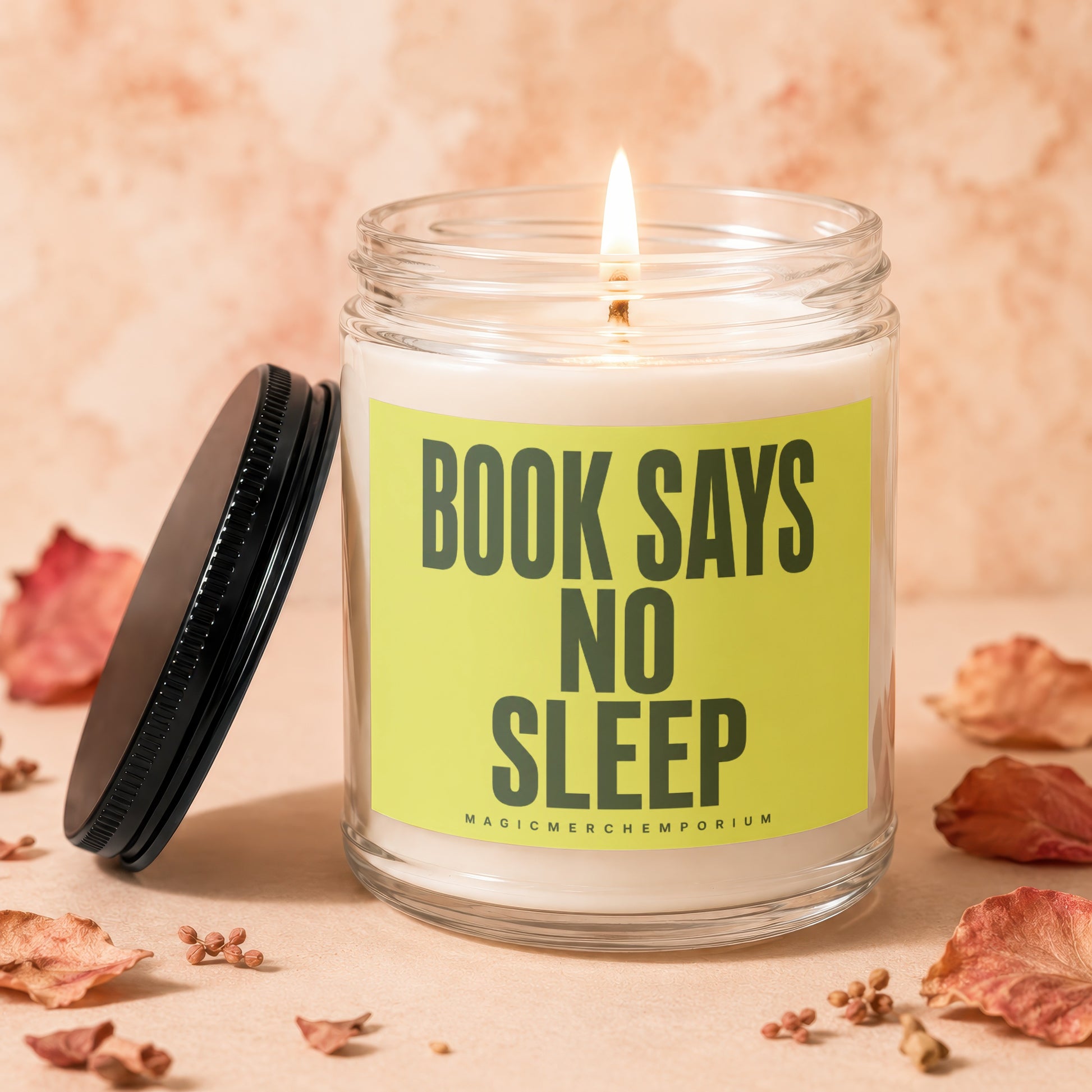 Candle with lit wick on a light brown surface, reads "BOOK SAYS NO SLEEP."