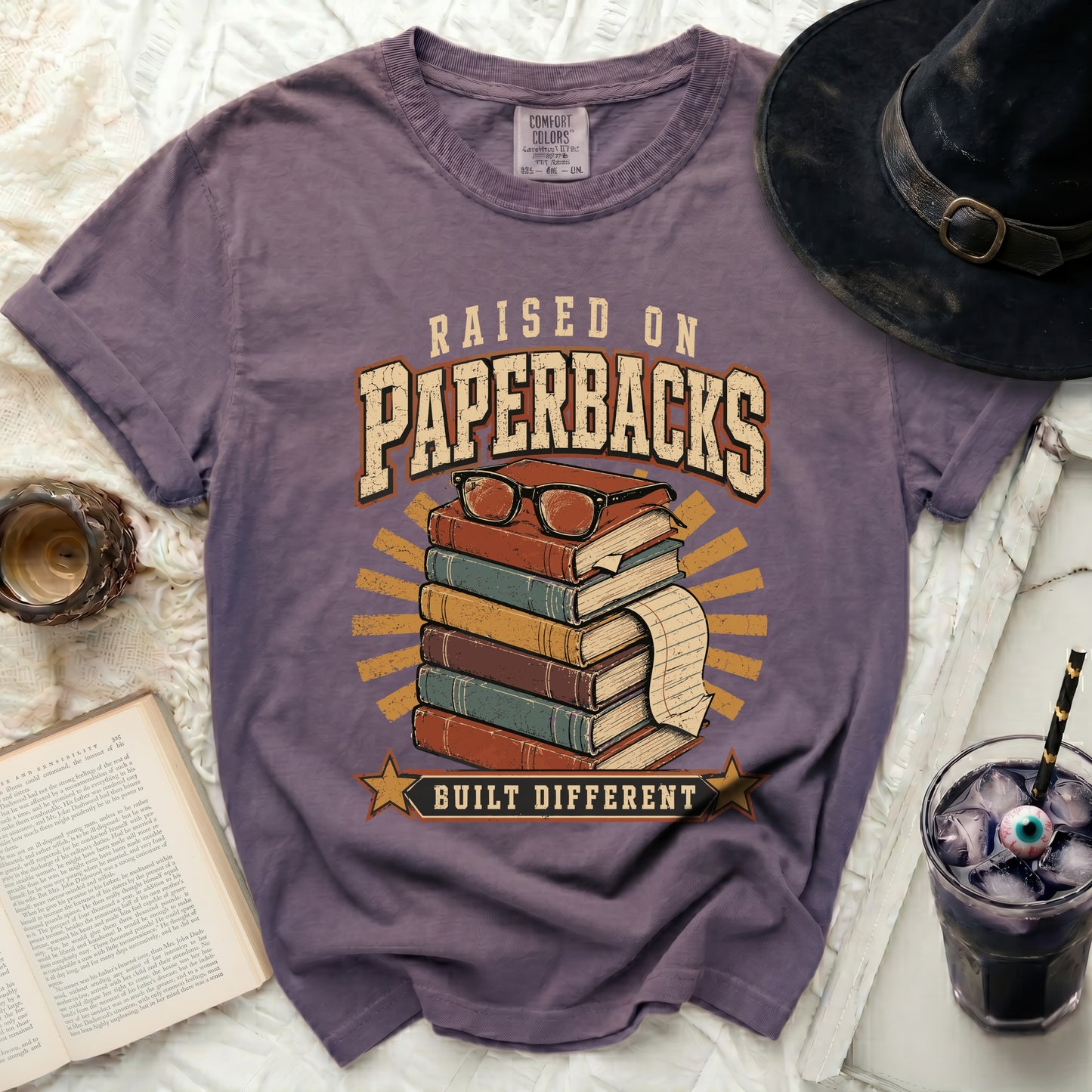 Purple t-shirt with "Raised on Paperbacks Built Different" text graphic.