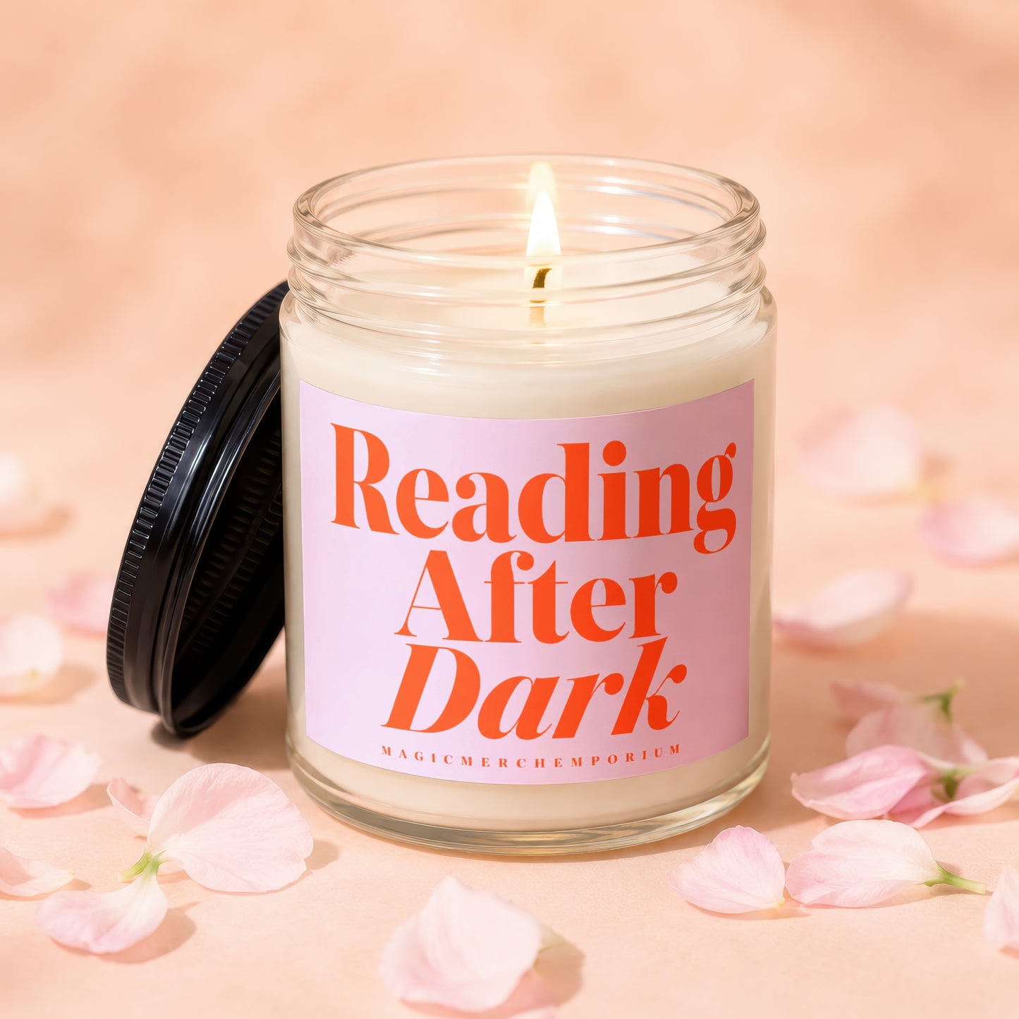 Lit glass jar candle with pink label reading "Reading After Dark" scattered with petals.