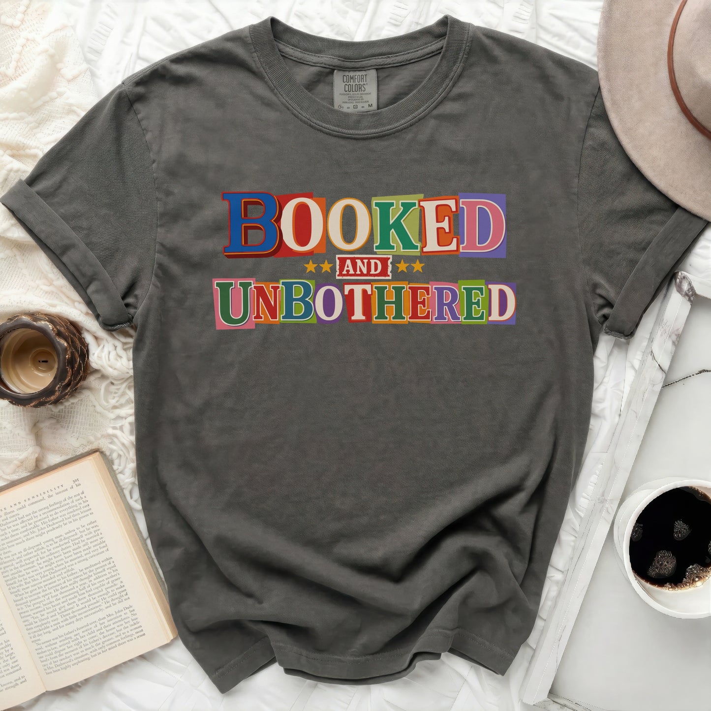 Dark gray t-shirt with "BOOKED AND UNBOTHERED" in colorful block letters.