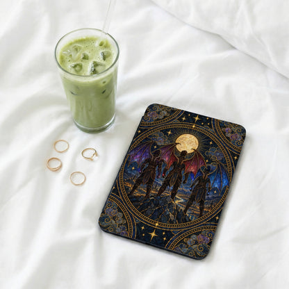 An e-reader with an ornate fantasy dragon illustration rests on white sheets next to rings and iced matcha.