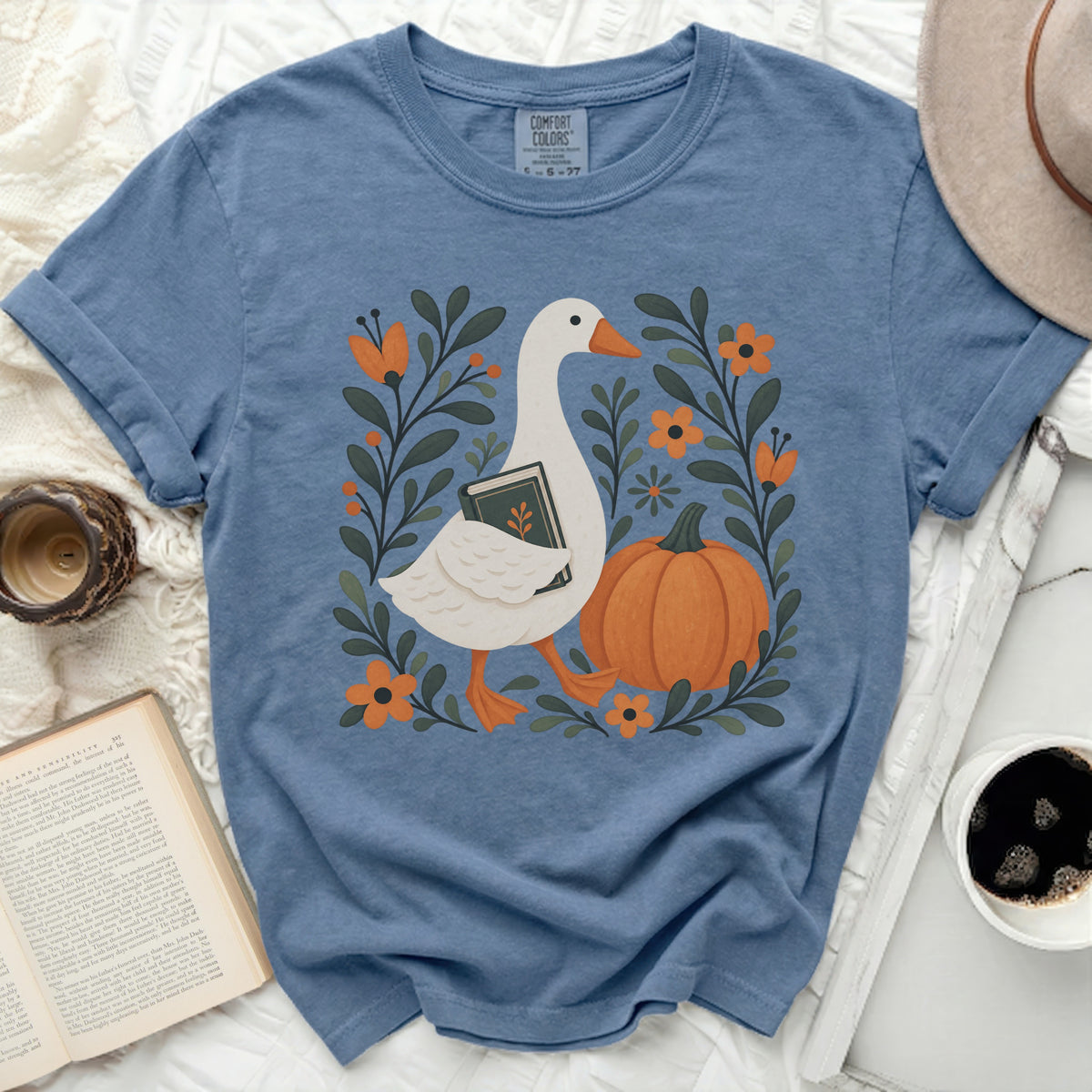 Blue t-shirt with goose, book, pumpkin, and floral design.