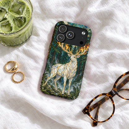 An ornate smartphone case featuring a white deer in a forest, resting on white fabric beside glasses, rings, and a glass of iced green tea.