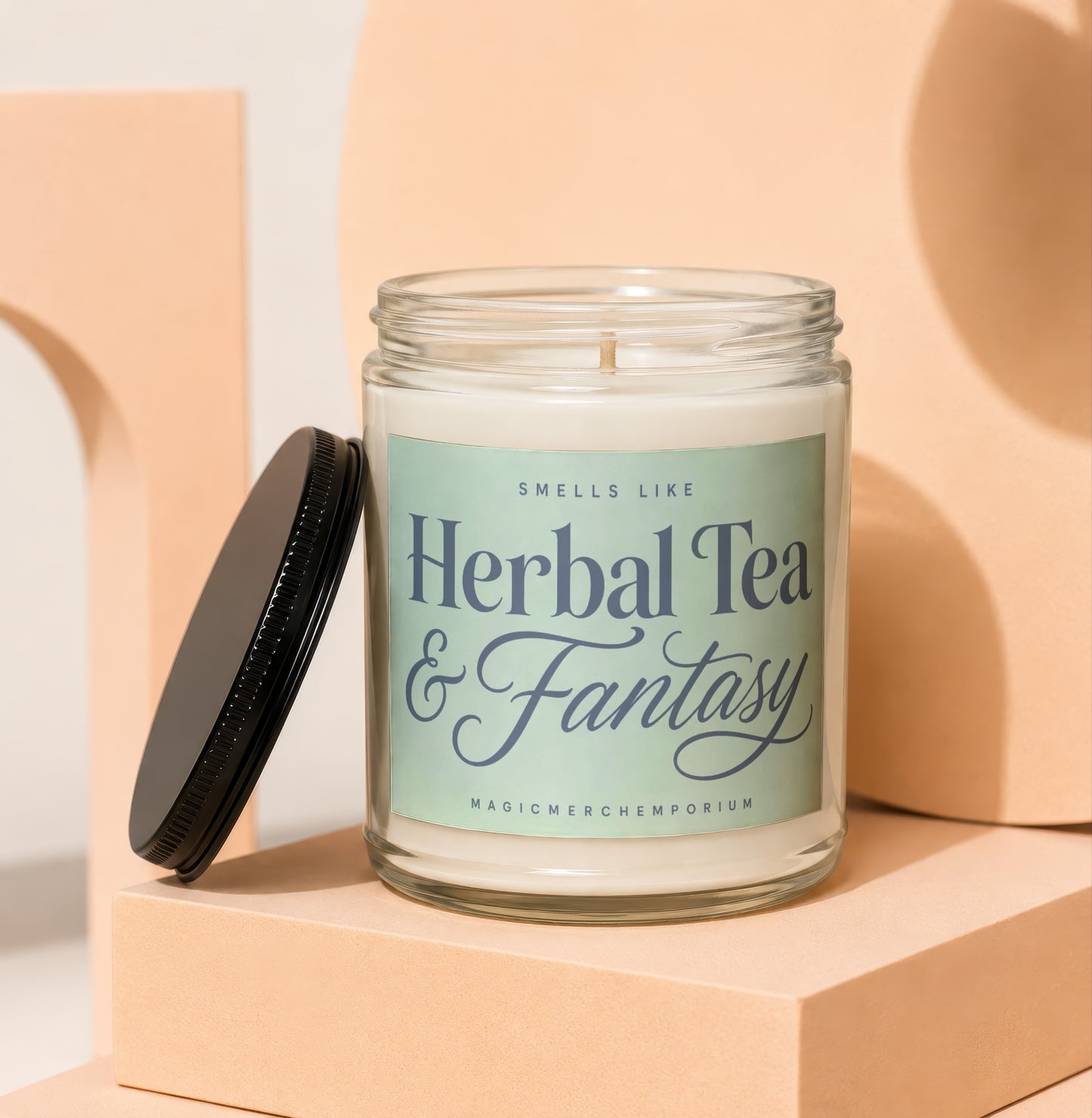 Glass candle with black lid, reads "Smells Like Herbal Tea & Fantasy"