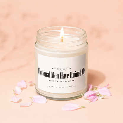 Lit candle in glass jar with label "Fictional Men Have Ruined Me" surrounded by petals.