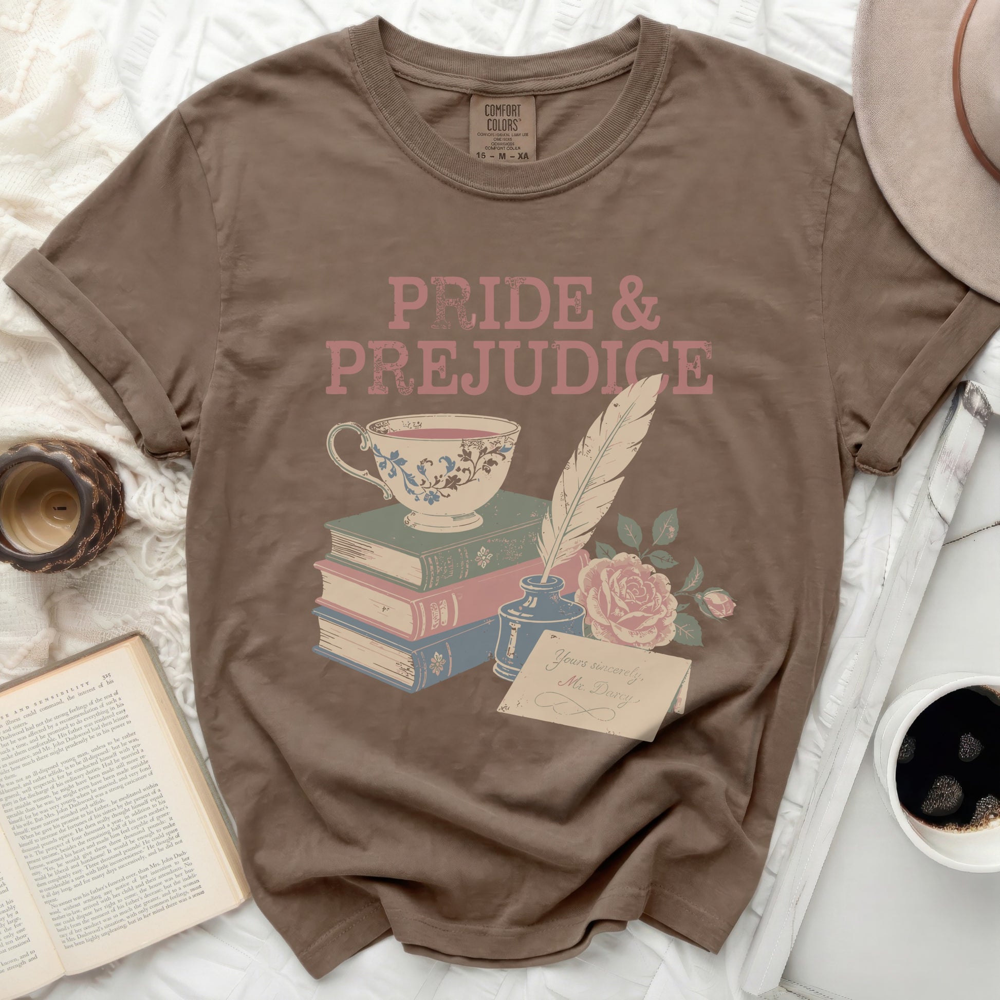 "Pride & Prejudice" graphic tee with tea cup, books, quill, and rose on a brown t-shirt.