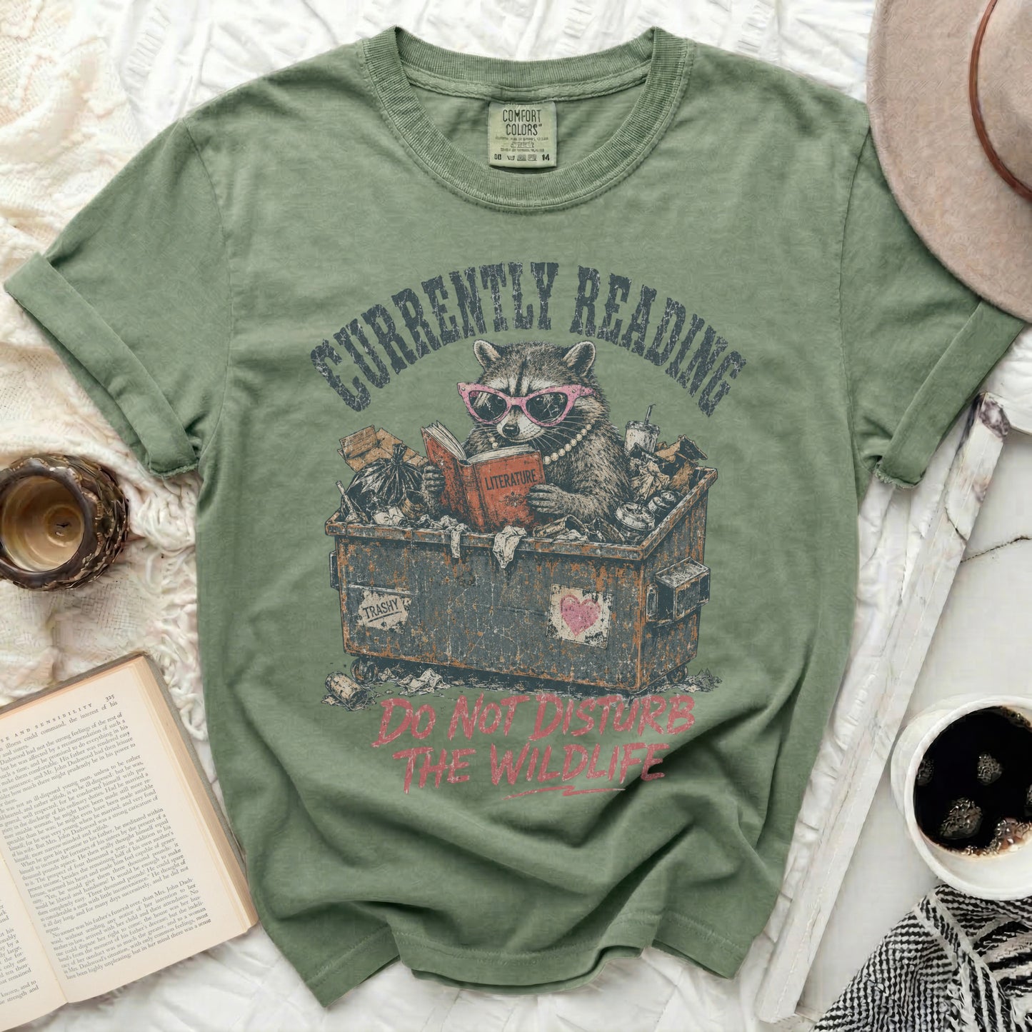 Green t-shirt with raccoon reading in trash, "Currently Reading Literature".