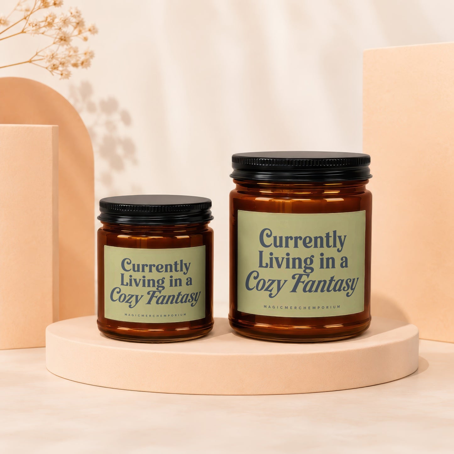 Two amber glass candles with black lids, labeled "Currently Living in a Cozy Fantasy".
