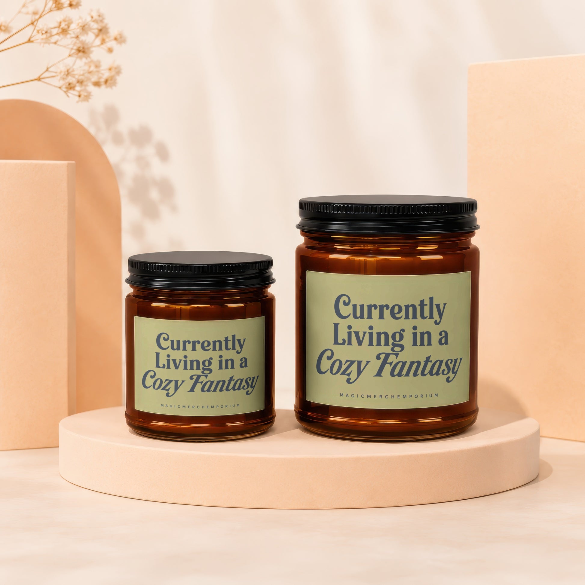 Two amber glass candles with black lids, labeled "Currently Living in a Cozy Fantasy".