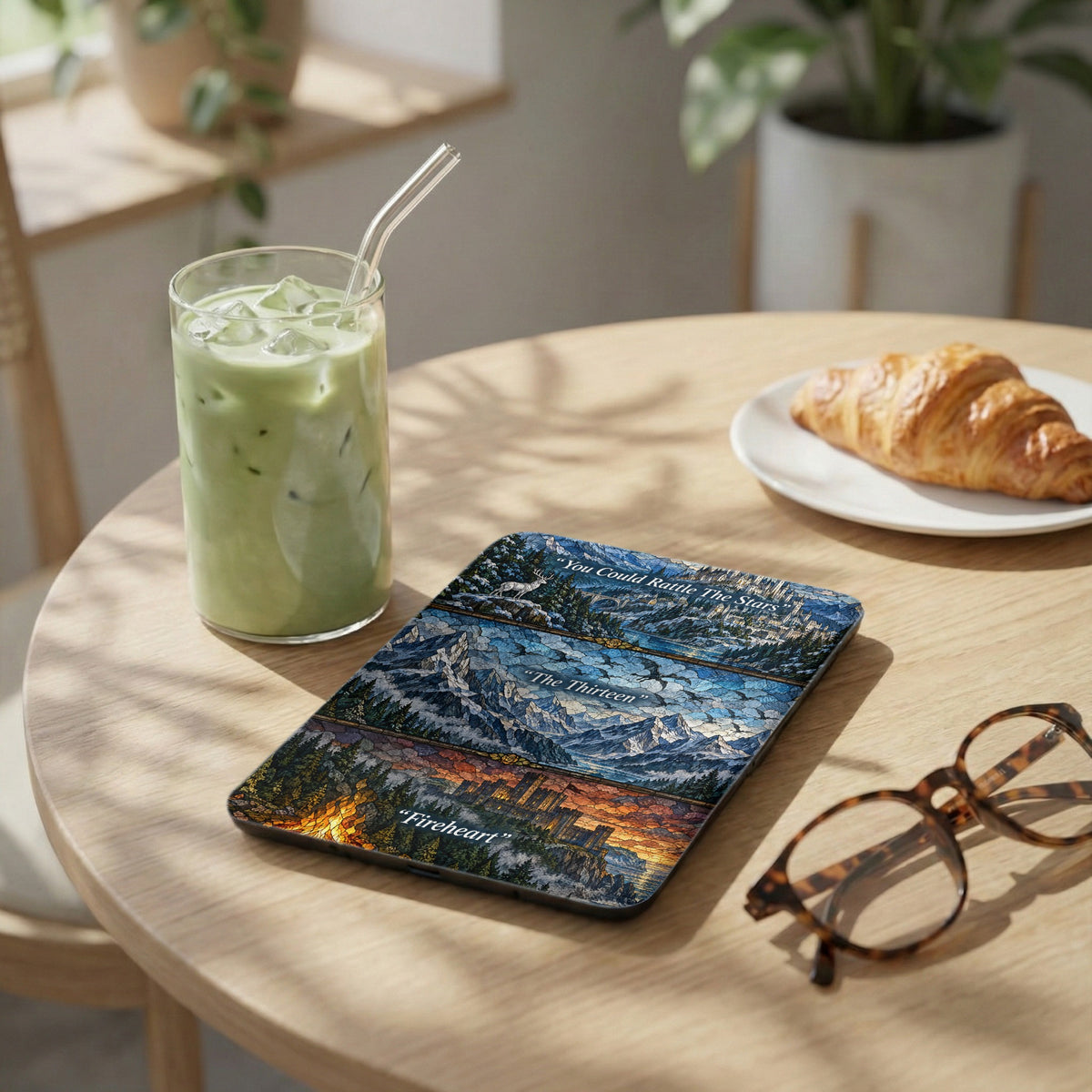 A Kindle skin featuring fantasy artwork with three horizontal panels showing castles and mountains, placed on a wooden table.