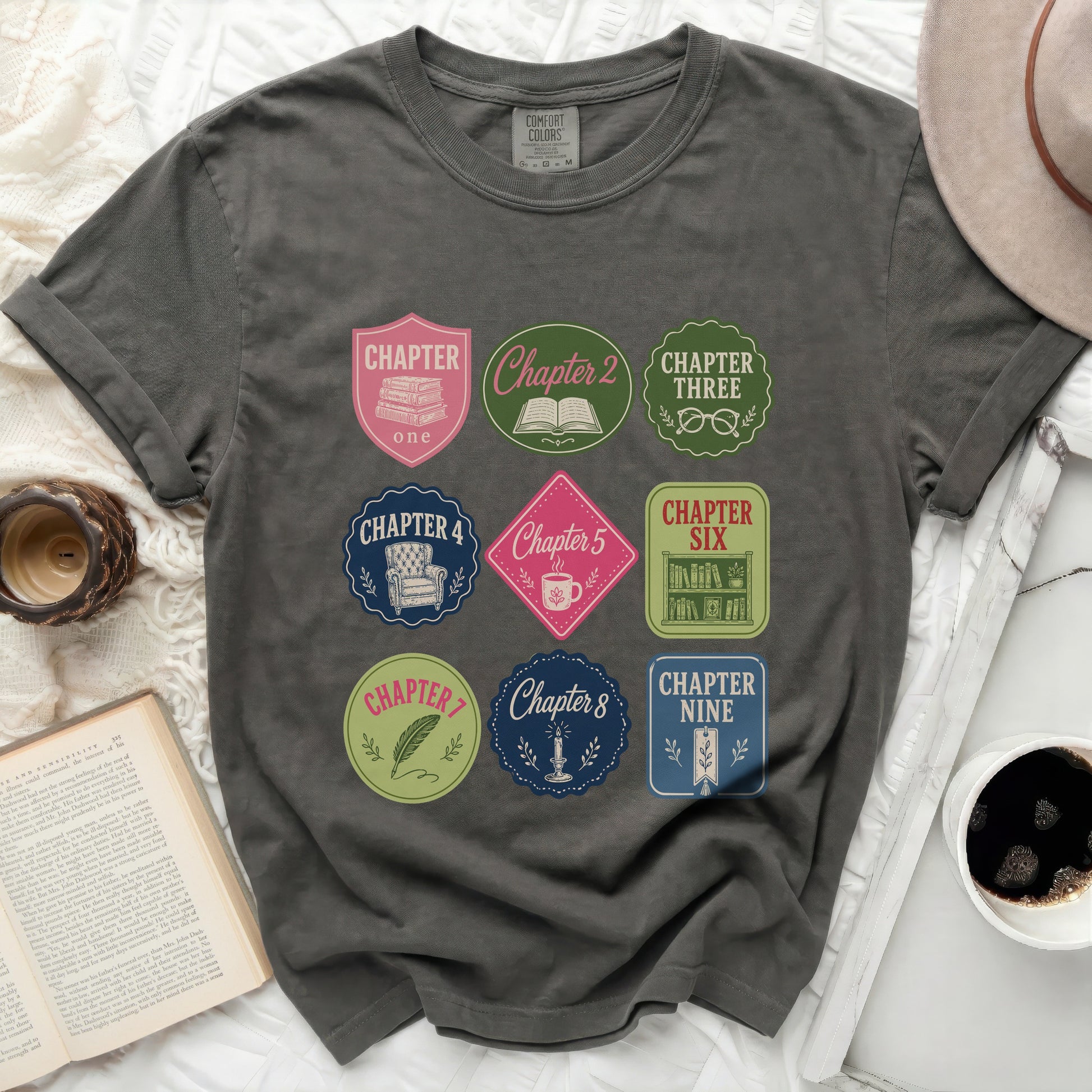 Dark gray t-shirt with circular "Chapter" patches featuring book and coffee cup designs.