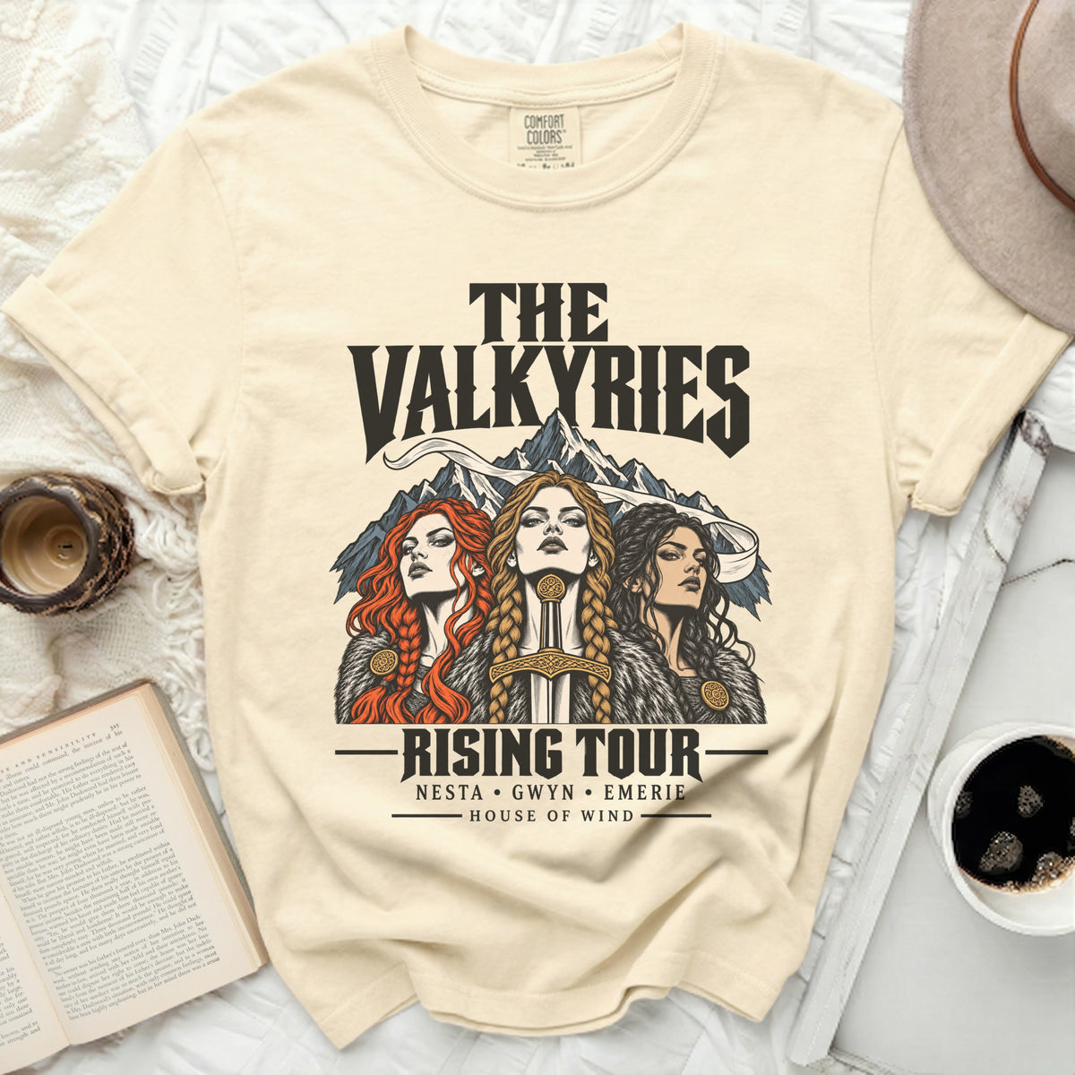 Cream t-shirt with "The Valkyries Rising Tour" graphic featuring three women and mountains.