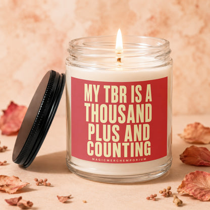 Lit candle in glass jar with red label reading "MY TBR IS A THOUSAND PLUS AND COUNTING".