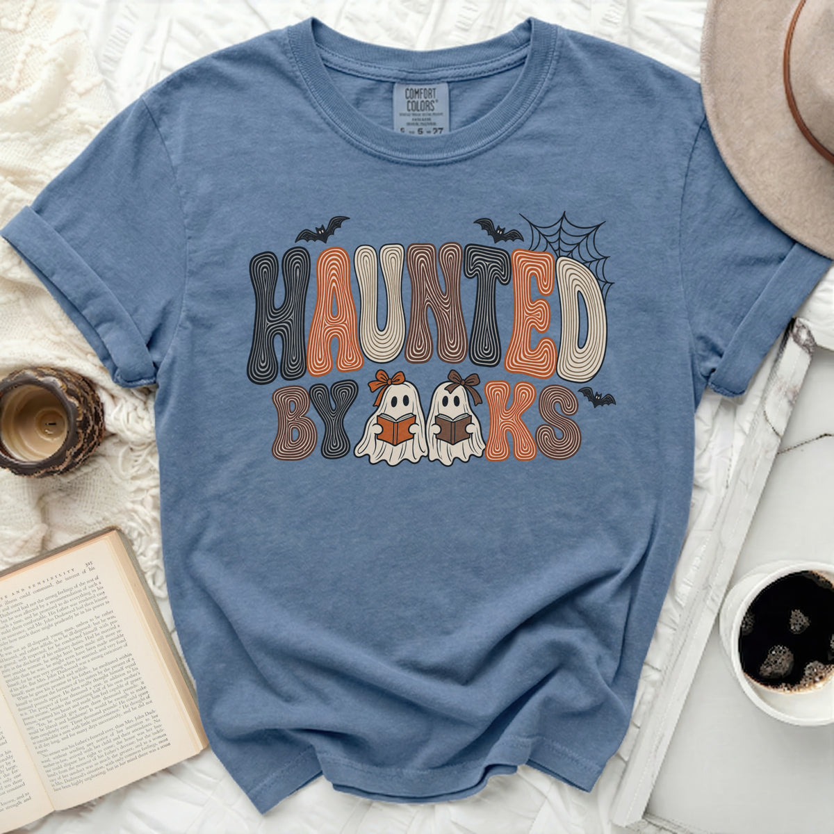 Blue t-shirt with "Haunted by Books" Halloween graphic and two ghosts reading.