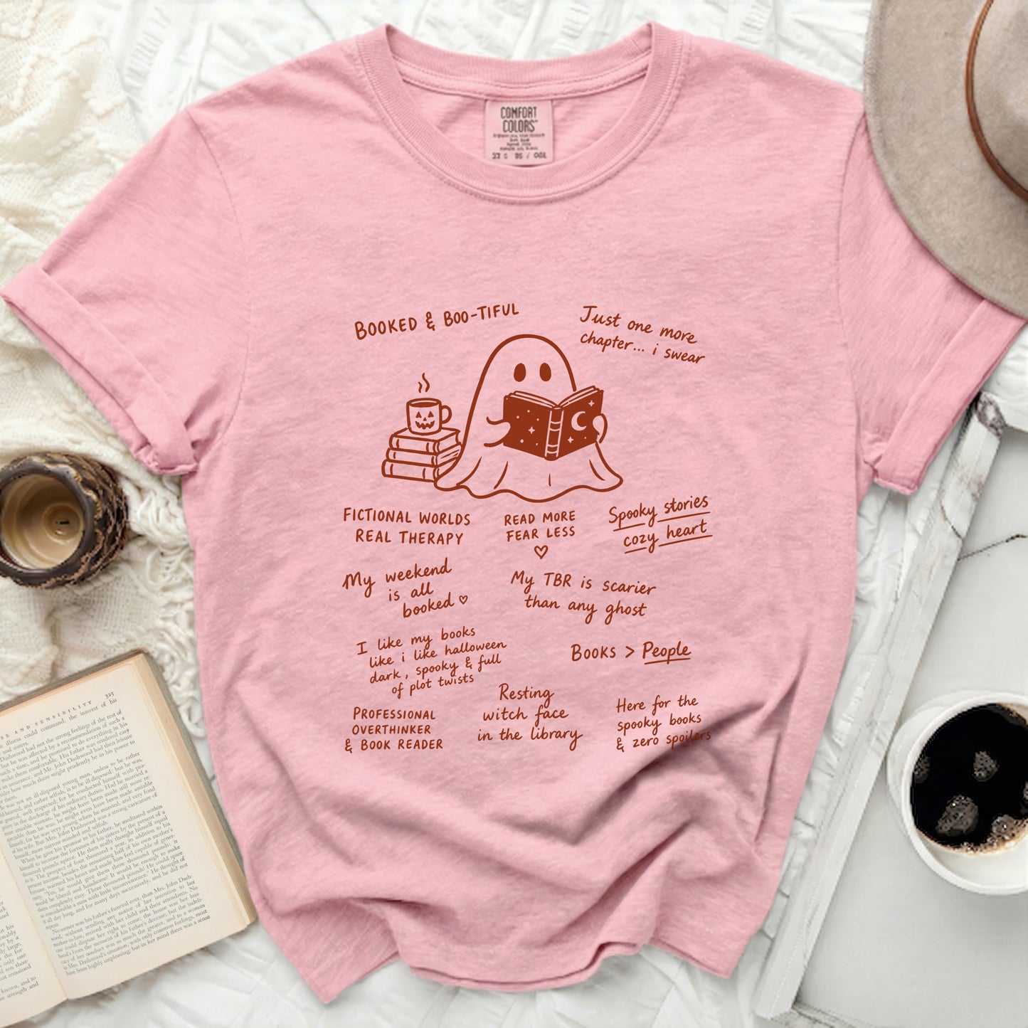 Pink t-shirt with a cartoon ghost reading a book and drinking coffee.
