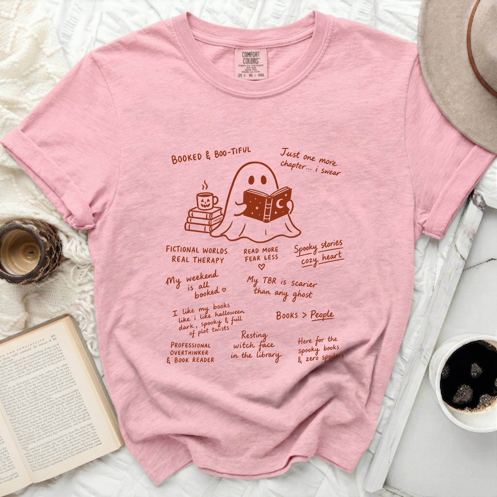 Pink t-shirt with a cartoon ghost reading a book and drinking coffee.