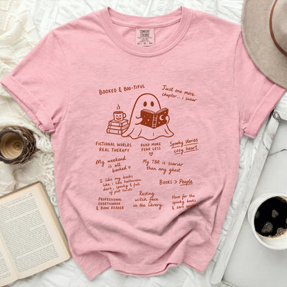 Pink t-shirt with a cartoon ghost reading a book and drinking coffee.