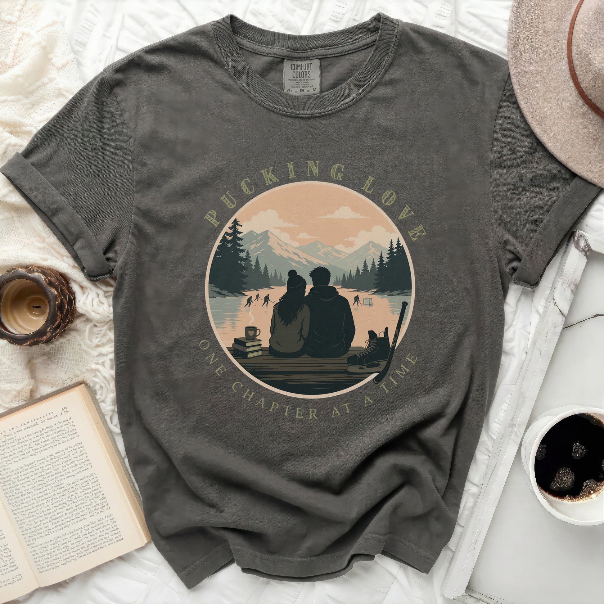 Dark grey t-shirt with circular graphic of couple ice skating, text "PUCKING LOVE ONE CHAPTER AT A TIME".