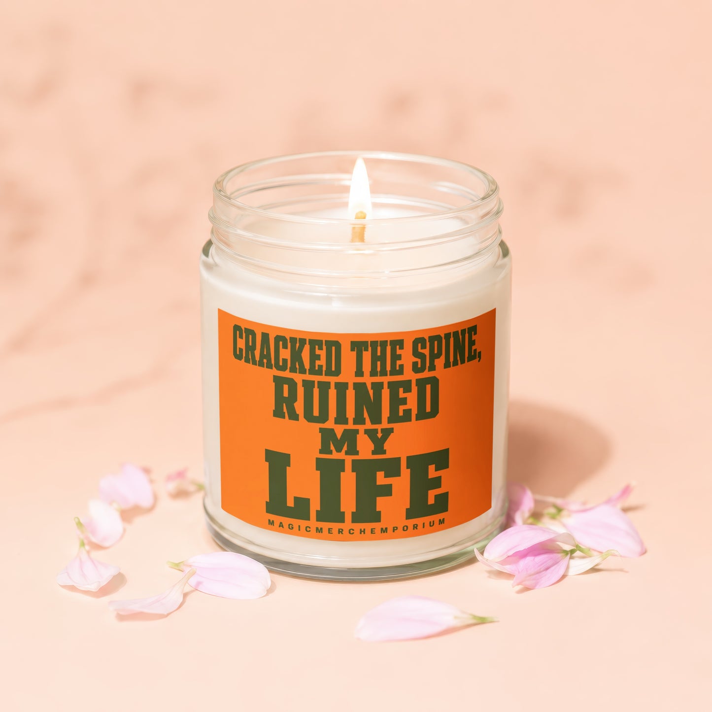 Candle with text "Cracked the spine, ruined my life" and "MagicMerchEmporium".