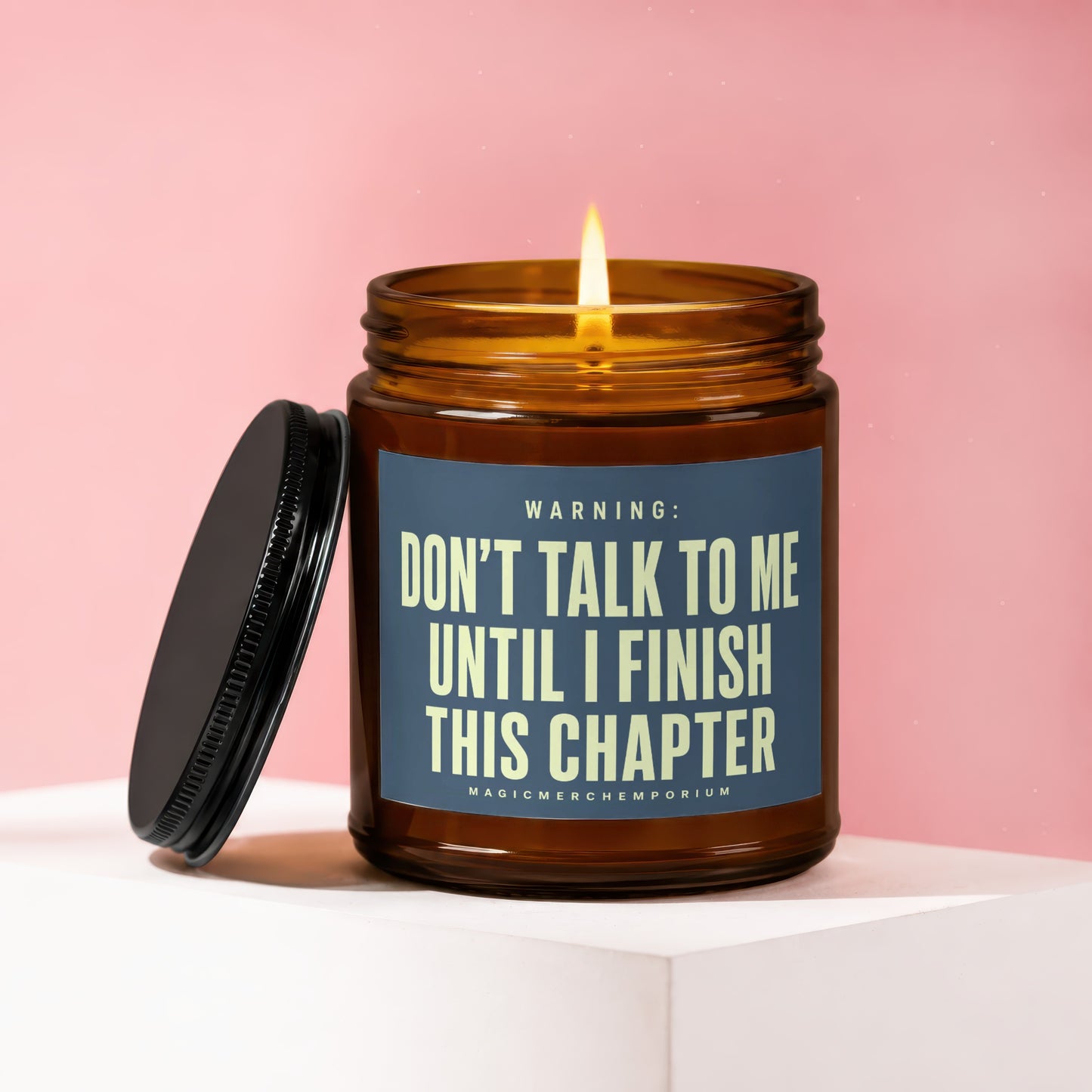 Amber candle with lit wick on blue label reading "Don't talk to me until I finish this chapter".