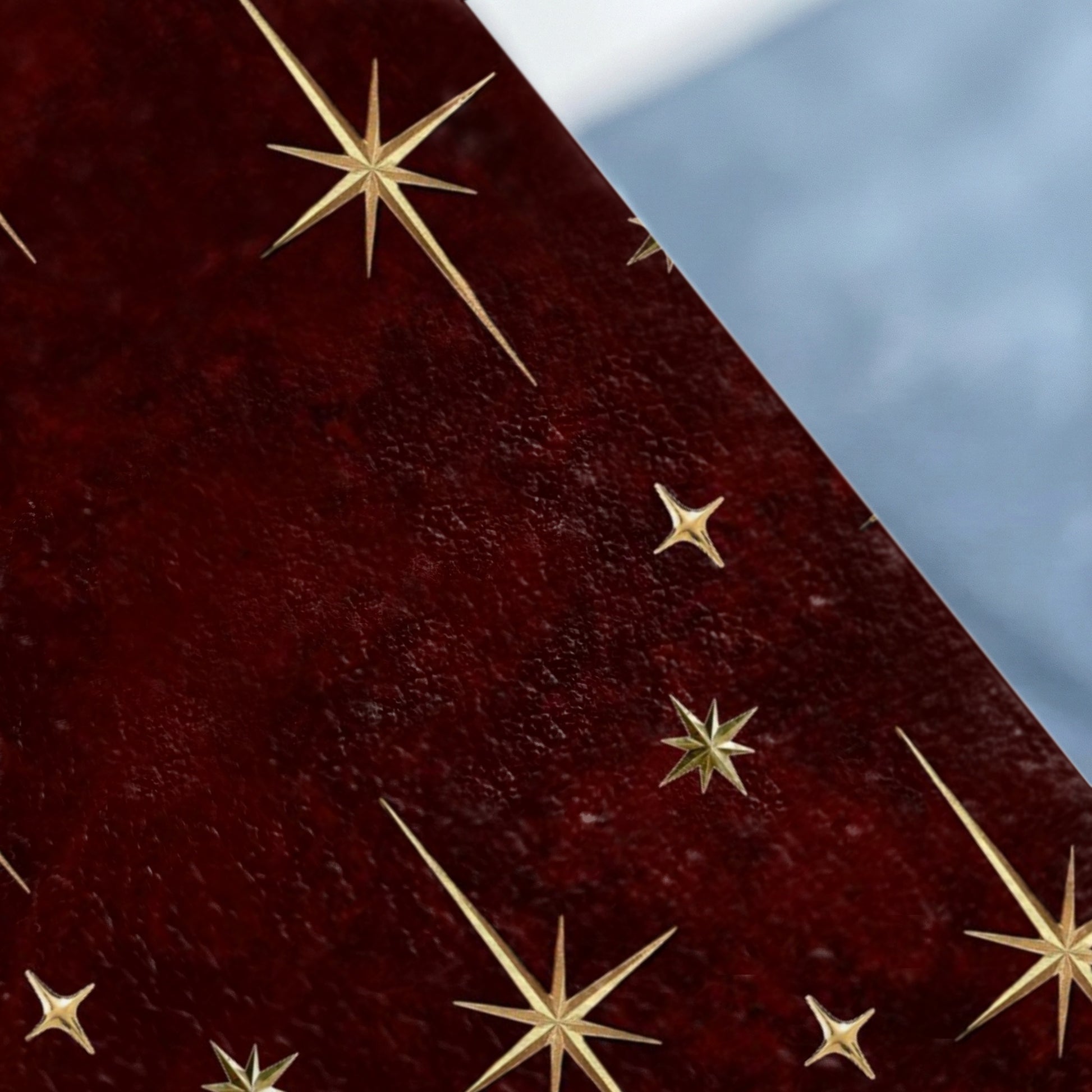 Dark red textured surface with scattered gold starburst designs and a blurred light blue background.