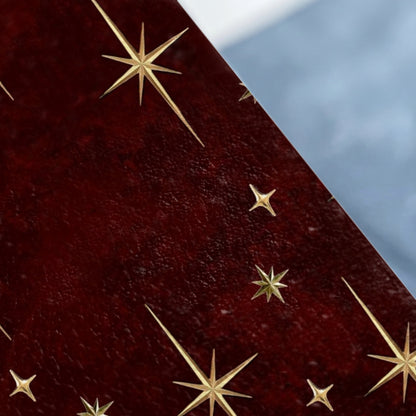 Dark red textured surface with scattered gold starburst designs and a blurred light blue background.