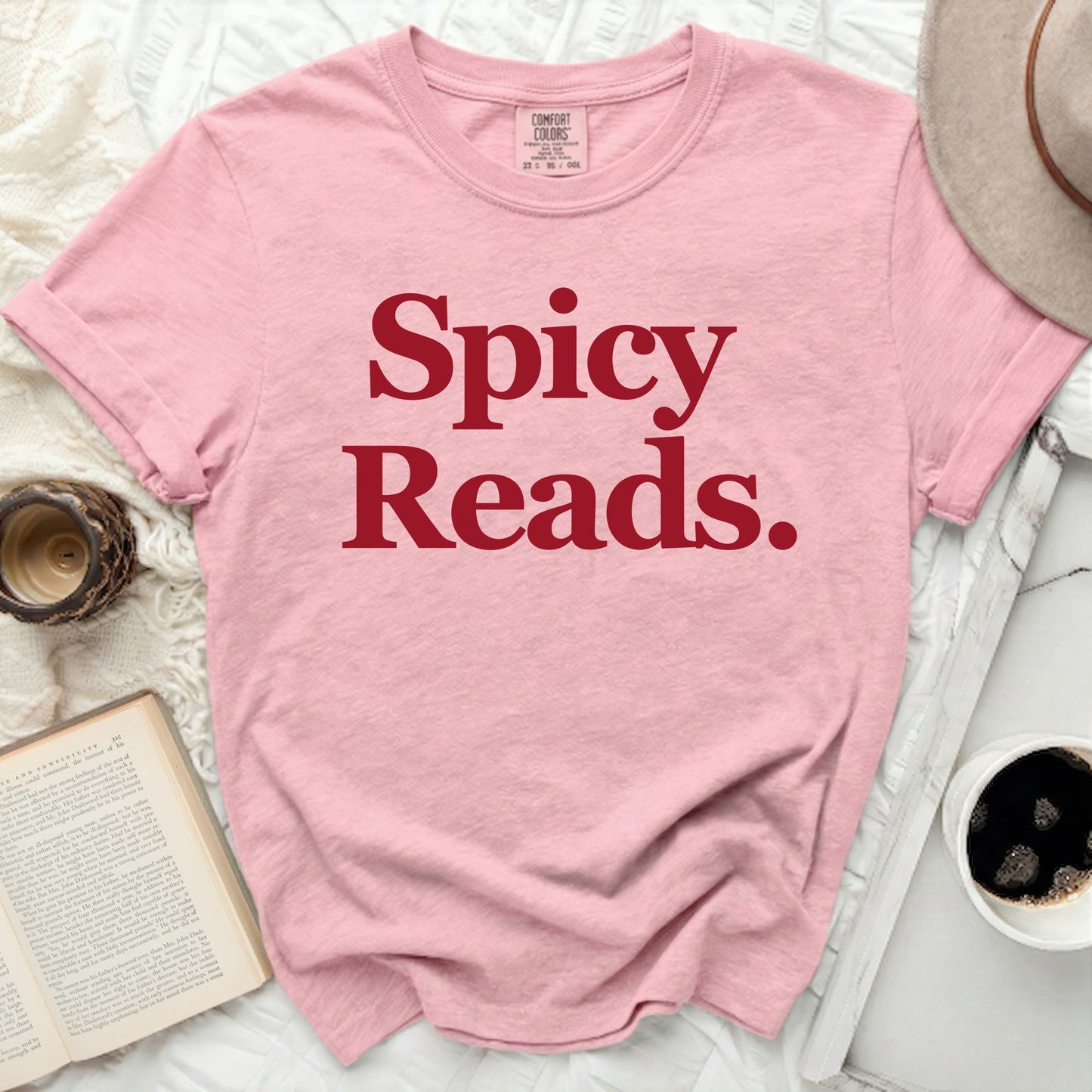 Pink shirt with red text "Spicy Reads.", book, coffee, and hat.