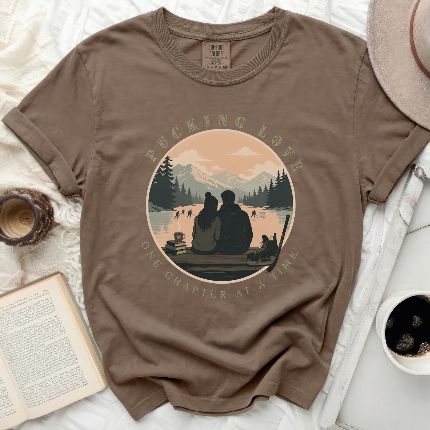 Brown t-shirt with circular graphic of couple ice skating, mountains, and text.
